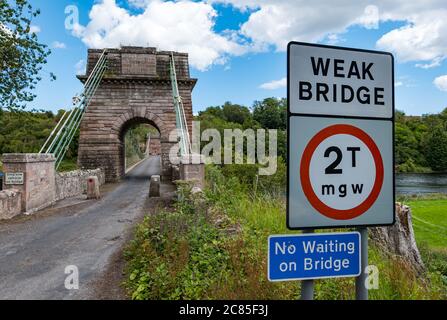 River Tweed, Englisch/Schottische Grenze, Großbritannien, 21. Juli 2020. 200 Jahre Union Bridge: Die Brücke feiert am 26. Juli ihr 200-jähriges Bestehen. Es war die erste Fahrzeugaufhängung Brücke in Großbritannien. Zur Zeit ihrer Errichtung war sie mit 137 m die längste schmiedeeiserne Hängebrücke der Welt. Es wird immer noch regelmäßig von Fußgängern, Radfahrern und Autos verwendet, aber Autos müssen es zu einer Zeit überqueren. Diese Ansicht ist von der schottischen Grenze mit einem Zeichen Warnung vor einer schwachen Brücke Stockfoto