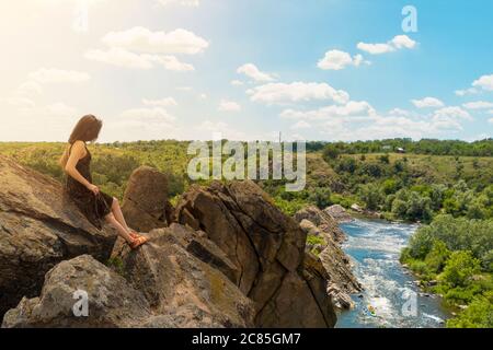 Eine junge Frau sitzt auf einem Felsen und blickt auf eine malerische Landschaft des südlichen Bug Flusses. Bug Guard Nationalpark in der Ukraine. Stock Foto.