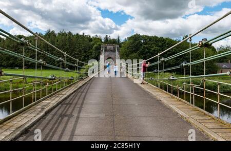 River Tweed, Englisch/Schottische Grenze, Großbritannien, 21. Juli 2020. 200 Jahre Union Bridge: Die Brücke feiert am 26. Juli ihr 200-jähriges Bestehen. Es war die erste Fahrzeugaufhängung Brücke in Großbritannien. Zur Zeit ihrer Errichtung war sie mit 137 m die längste schmiedeeiserne Hängebrücke der Welt. Es wird immer noch regelmäßig von Fußgängern, Radfahrern und Autos verwendet, aber Autos müssen es zu einer Zeit überqueren. Diese Ansicht ist von der englischen Grenze. Die Leute gehen über die Brücke Stockfoto