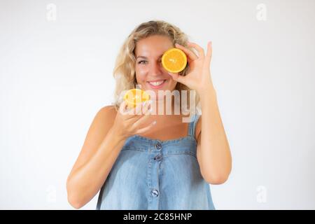 Hübsche blonde Frau in blauem Kleid lächelt mit einer Orange im Auge Stockfoto