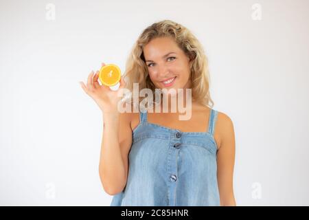 Hübsche blonde Frau in blauem Kleid lächelt mit einer Orange in der Hand Stockfoto