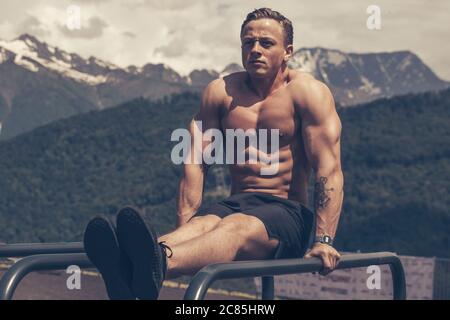 Portrait von blonden Bodybuilder tun Trizeps Dips auf parallelen Bars im Park Ausübung im Freien Fitnessstudio im Sommer Hochland Landschaft Stockfoto