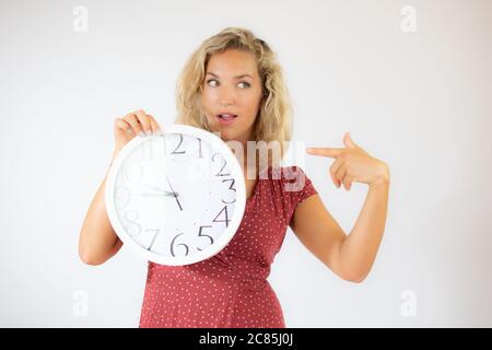 Hübsche blonde Frau in rotem Kleid zeigt eine große Uhr Stockfoto