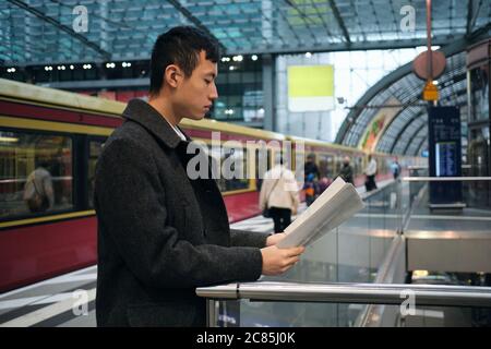 Seitenansicht des asiatischen Geschäftsmannes, der an der U-Bahn-Station aufmerksam Zeitung liest Stockfoto