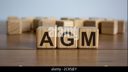 Konzept Wort "AGM" - Akronym von Worten "Jahreshauptversammlung" auf Würfel auf einem schönen Holztisch. Weißer Hintergrund. Geschäftskonzept. Stockfoto