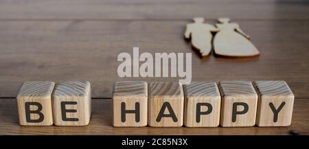 Sei glücklich Buchstaben Würfel auf Holzboden. Holzfiguren von Mann und Frau. Stockfoto
