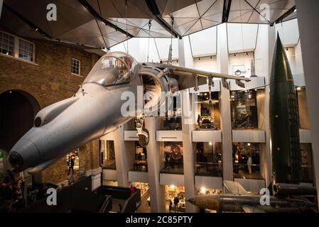 LONDON, Großbritannien — Ein Harrier Jump Jet hängt über der Haupthalle des Imperial war Museum in London. Das ikonische britische Flugzeug, bekannt für seine vertikalen Start- und Landemöglichkeiten, dient als Herzstück der umfangreichen Sammlung militärischer Artefakte und Ausstellungen, die sich mit der modernen Kriegsführung und ihren Auswirkungen auf die Gesellschaft befassen. Stockfoto