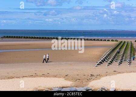 Menschen, die am New Brighton Beach am Wirral in der Sonne neben den massiven Betonbrechern Meer Verteidigung schlendern. Stockfoto