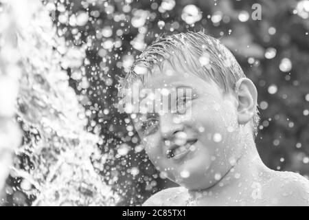 Schöne Graustufenaufnahme eines jungen kaukasischen Jungen, der mit spielt Wasser in einem Hof und Spaß haben Stockfoto