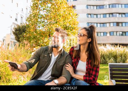 Ein Paar sitzt auf einer Parkbank in der Stadt versucht, Orientierung mit Hilfe des Smartphones zu bekommen. Stockfoto