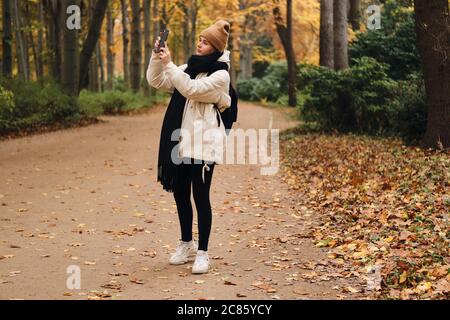 Schönes Mädchen zu Fuß durch Herbst Park und Fotos auf dem Handy Stockfoto