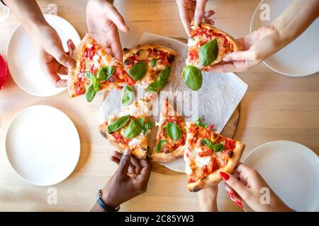 High-Angle-Aufnahme von nicht erkennbaren Mischrennen Menschen Hände jeder greifen ein Stück Pizza Stockfoto