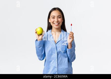 Morgen, aktiv und gesund Lebensstil und Home-Konzept. Lächelnd schöne asiatische Mädchen zeigt Zahnbürste und grünen Apfel, haben perfekte weiße Zähne und Stockfoto