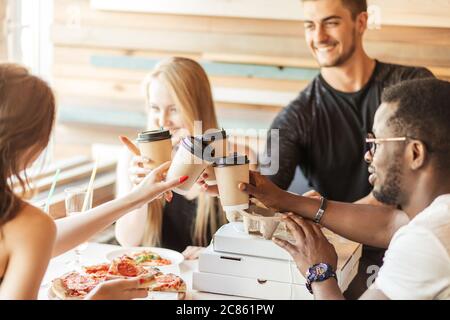 Gruppe junger multirassischer Freunde, die in einem Café herumhängen. Junge Männer und Frauen treffen sich in einem Café Spaß haben, Pizza essen und Kaffee trinken Stockfoto