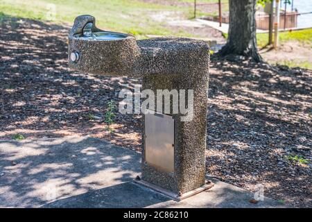 Alte kieselbedeckte Trinkwasserbrunnen noch in Betrieb mit einer Edelstahlschale sitzen auf einem Zementblock in einem Park an einem sonnigen Tag im Sommer Stockfoto