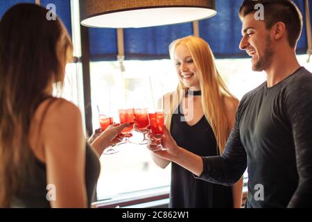 Junge, fröhliche Mitarbeiter gratulieren ihrem Kollegen mit neuer Position. Trinken im Restaurant, Toasten mit rosa Getränke neuen Termin. Stockfoto