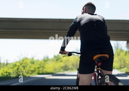 Radfahrer, die auf offener Straße ein Fahrrad fahren, um den Sonnenuntergang-Sportler, bärtigen Radler, Fahrten auf der Autobahn auf einem Sportfahrrad. Unter der Brücke. Im Freien. S Stockfoto