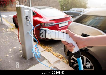 Hand mit Ladegerät auf einem Hintergrund von Elektroauto Stockfoto