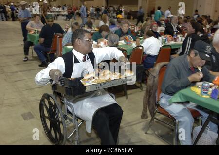 San Antonio, Texas USA, 24. November 2005: Ein afroamerikanischer Mann im Rollstuhl serviert beim jährlichen Raul Jiminez Thanksgiving Dinner, bei dem mehr als 25.000 Mahlzeiten am Thanksgiving Day für ältere Menschen, Obdachlose, Arme und Vertriebene aus Südtexas serviert werden. Die Veranstaltung, die vom verstorbenen Restaurantbesitzer Raul Jiminez ins Leben gerufen wurde, findet im 26. Jahr statt. ©Bob Daemmrich Stockfoto