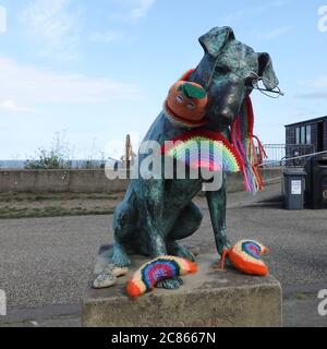 Aldeburgh, Suffolk - 21. Juli 2020: Snooks der Hund. Eine Bronzestatue, die als Denkmal für einen Hausarzt errichtet wurde. Verziert mit gestrickten Regenbögen für den NHS. Stockfoto