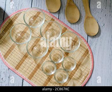 Draufsicht auf neun leere Glasschüsseln und drei Holzlöffel auf einem weißen Holzbrett Hintergrund. Stockfoto