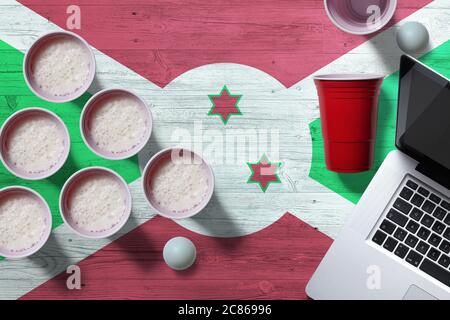 Burundi Flagge Konzept mit Kunststoff Bier Pong Tassen und Laptop auf nationalen Holztisch, Draufsicht. Bier Pong Spiel. Stockfoto