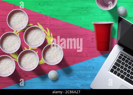 Eritrea Flagge Konzept mit Kunststoff Bier Pong Tassen und Laptop auf nationalen Holztisch, Draufsicht. Bier Pong Spiel. Stockfoto