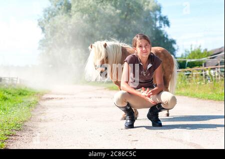 Freundschaft und Vertrauen. Lächelndes Teenager-Mädchen sitzt in der Nähe niedlichen kleinen shetland Pony. Sommerzeit im Freien horizontales Bild. Stockfoto