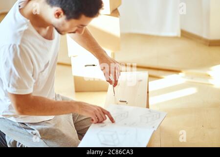 Frustrierter Mann, der Anweisungen liest und Möbel zusammenführt. DIY, neues Zuhause Stockfoto