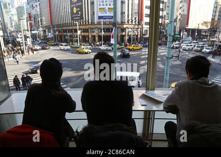 Kreuzung mit 4 Viererteiler im Ginza-Viertel, Tokio. Drei Männer schauen durch das Fenster einer Bar auf die Kreuzung. Stockfoto