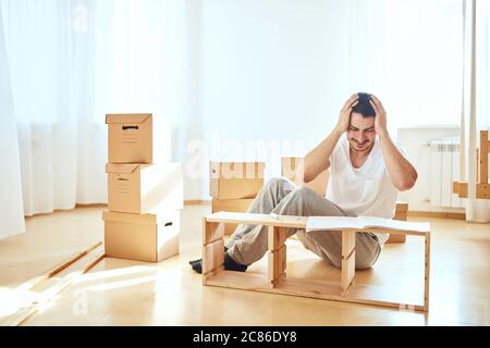 Konzentrierter junger Mann, der Anweisungen liest, um Möbel zu Hause zu montieren Stockfoto