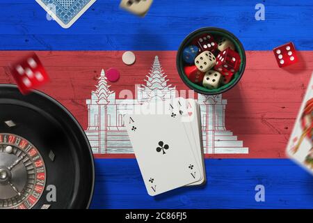 Kambodscha Casino Thema. Asse im Pokerspiel, Karten und Chips auf rotem Tisch mit Nationalflagge Hintergrund. Glücksspiel und Wetten. Stockfoto