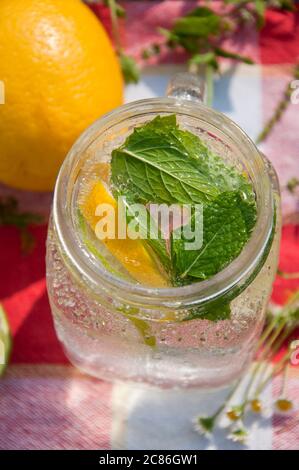 Kaltes Erfrischungsgetränk im Glasgefäß mit Zitronenscheiben und Limetten. Dekoriert mit frischen Minzkräutern auf Holzhintergrund. Stockfoto