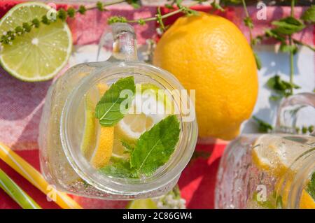 Kaltes Erfrischungsgetränk im Glasgefäß mit Zitronenscheiben und Limetten. Dekoriert mit frischen Minzkräutern auf Holzhintergrund. Stockfoto