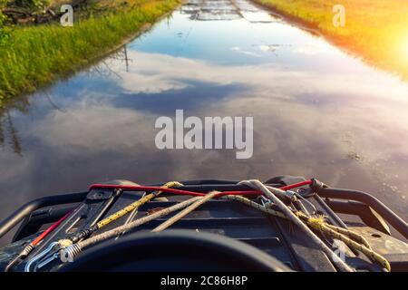 ATV Quadbike Reiten durch überflutet nach schweren Sturm regen Straße mit landschaftlich klaren blauen Wolke Himmel Reflexion im Wasser Pudle. Abenteuerreise. Weg zu Stockfoto