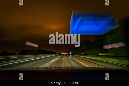 Die Langzeitaufnahme einer Autobahn in der Nacht während der Fahrt über eine deutsche Autobahn und ein typisches blaues Schild. Stockfoto