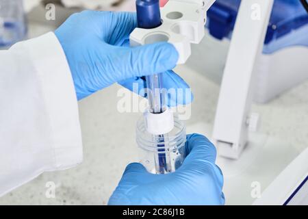 Frau in einem Gummihandschuh mit einer Glaselektrode zur Messung des pH-Wertes der Lösung mit einem pH-Messgerät. Labor für analytische oder elektrochemische Untersuchungen. Stockfoto