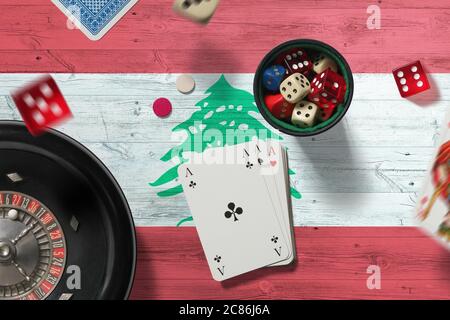 Libanon Casino Thema. Asse im Pokerspiel, Karten und Chips auf rotem Tisch mit Nationalflagge Hintergrund. Glücksspiel und Wetten. Stockfoto