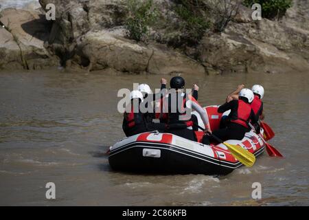 Die Teammitglieder rudern im Rafting Boot den trüben Fluss hinunter während der Sommerzeit. Komplette Ausrüstung mit Helm enthalten Stockfoto