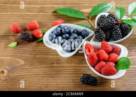 Seasonal forest fruits, raspberries, blueberries, blackberries in the white bowls, on the wooden background. Stockfoto