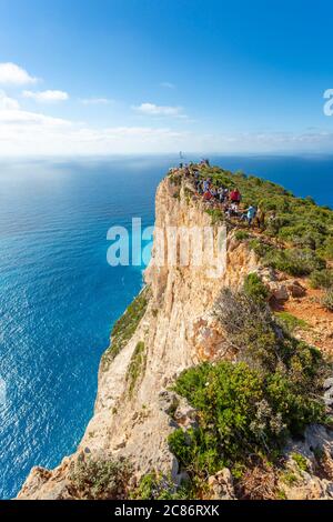 Touristen stehen am Rand einer hohen Klippe über Navagio Beach (Shipwreck Beach) in Zakynthos, Griechenland Stockfoto