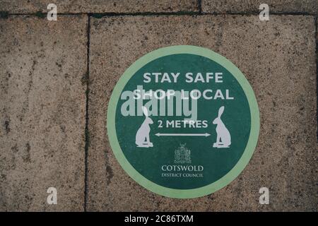 Stow-on-the-Wold, Großbritannien - 6. Juli 2020: Stay Safe Shop Lokale und 2 Meter soziale distanzierende grüne Zeichen auf einem Bürgersteig einer Straße in Stow-on-the-Wold, ein m Stockfoto
