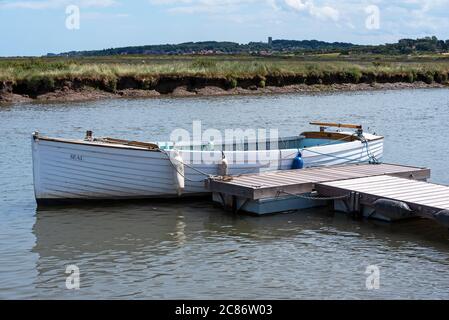 Morston Quay, Norfolk, Großbritannien. Weißer hölzerner Klinker gebaut Segeljollen Seal an den Liegeplätzen. Das Dorf Blakeney und der Turm der Blakeney Kirche in der Ferne sichtbar. Quelle: Stephen Bell/Alamy Stockfoto