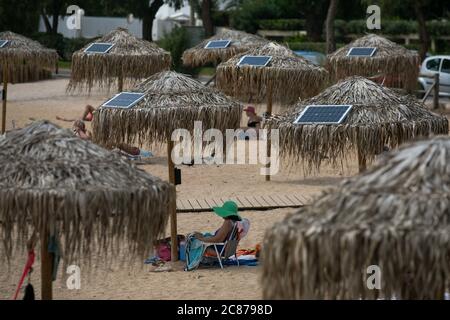 (200721) -- ATHEN, 21. Juli 2020 (Xinhua) -- das Foto vom 21. Juli 2020 zeigt Sonnenkollektoren auf Sonnenschirmen an einem öffentlichen Strand in der Nähe des Rathauses der Gemeinde Vari-Voula-Vouliagmeni im Süden Athens, Griechenland. Ab Dienstag sind die Dutzende von Sonnenschirmen, die entlang des Strandes verteilt sind, gemäß den sicheren Entfernungsmaßnahmen zum Schutz gegen COVID-19, mit einem System aus Solarmodulen und USB-Anschlüssen ausgestattet, das kostenlos und umweltfreundlich aufgeladen werden kann. Im Rahmen eines am Dienstag gestarteten Pilotprogramms werden Sonnenanbeter mit Hilfe von Solar e zu Energieeinsparungen beitragen Stockfoto