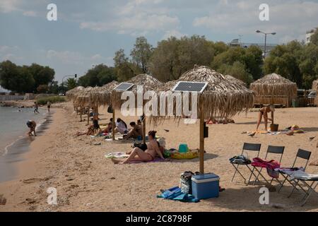 (200721) -- ATHEN, 21. Juli 2020 (Xinhua) -- das Foto vom 21. Juli 2020 zeigt Sonnenkollektoren auf Sonnenschirmen an einem öffentlichen Strand in der Nähe des Rathauses der Gemeinde Vari-Voula-Vouliagmeni im Süden Athens, Griechenland. Ab Dienstag sind die Dutzende von Sonnenschirmen, die entlang des Strandes verteilt sind, gemäß den sicheren Entfernungsmaßnahmen zum Schutz gegen COVID-19, mit einem System aus Solarmodulen und USB-Anschlüssen ausgestattet, das kostenlos und umweltfreundlich aufgeladen werden kann. Im Rahmen eines am Dienstag gestarteten Pilotprogramms werden Sonnenanbeter mit Hilfe von Solar e zu Energieeinsparungen beitragen Stockfoto