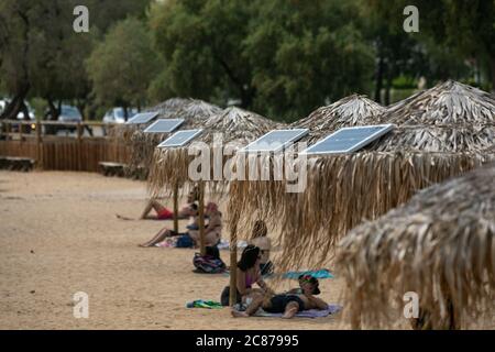 (200721) -- ATHEN, 21. Juli 2020 (Xinhua) -- das Foto vom 21. Juli 2020 zeigt Sonnenkollektoren auf Sonnenschirmen an einem öffentlichen Strand in der Nähe des Rathauses der Gemeinde Vari-Voula-Vouliagmeni im Süden Athens, Griechenland. Ab Dienstag sind die Dutzende von Sonnenschirmen, die entlang des Strandes verteilt sind, gemäß den sicheren Entfernungsmaßnahmen zum Schutz gegen COVID-19, mit einem System aus Solarmodulen und USB-Anschlüssen ausgestattet, das kostenlos und umweltfreundlich aufgeladen werden kann. Im Rahmen eines am Dienstag gestarteten Pilotprogramms werden Sonnenanbeter mit Hilfe von Solar e zu Energieeinsparungen beitragen Stockfoto