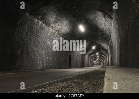 Monsal Trail Straße führt durch Grabstein Tunnel, aus dunkelgrauen Ziegeln, ein tief und Weitwinkel-Bild, leer und Kopierer Raum. Alter und rustikaler Tunnel. Stockfoto