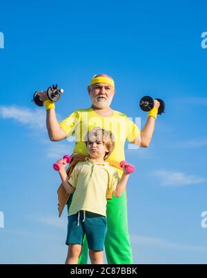 Sport- und Trainingskonzepte. Familiensport. Großvater und Sohn machen Übungen. Kind, das eine Hantel hebt. Lustige alte ältere Mann und Junge mit Stockfoto