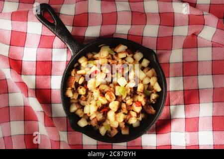 High-Angle-Schuss einer gusseisernen Pfanne mit Country-Stil Hash braunen Kartoffeln auf einem roten karierten Tischtuch mit warmen Seitenlicht. Stockfoto