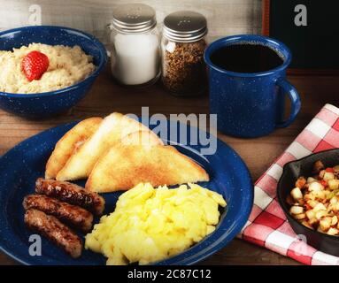 Ein rustikales Rührei-Frühstück auf einem rustikalen Holztisch mit Haferbrei, Kartoffeln und Kaffee mit warmer Beilage. Stockfoto